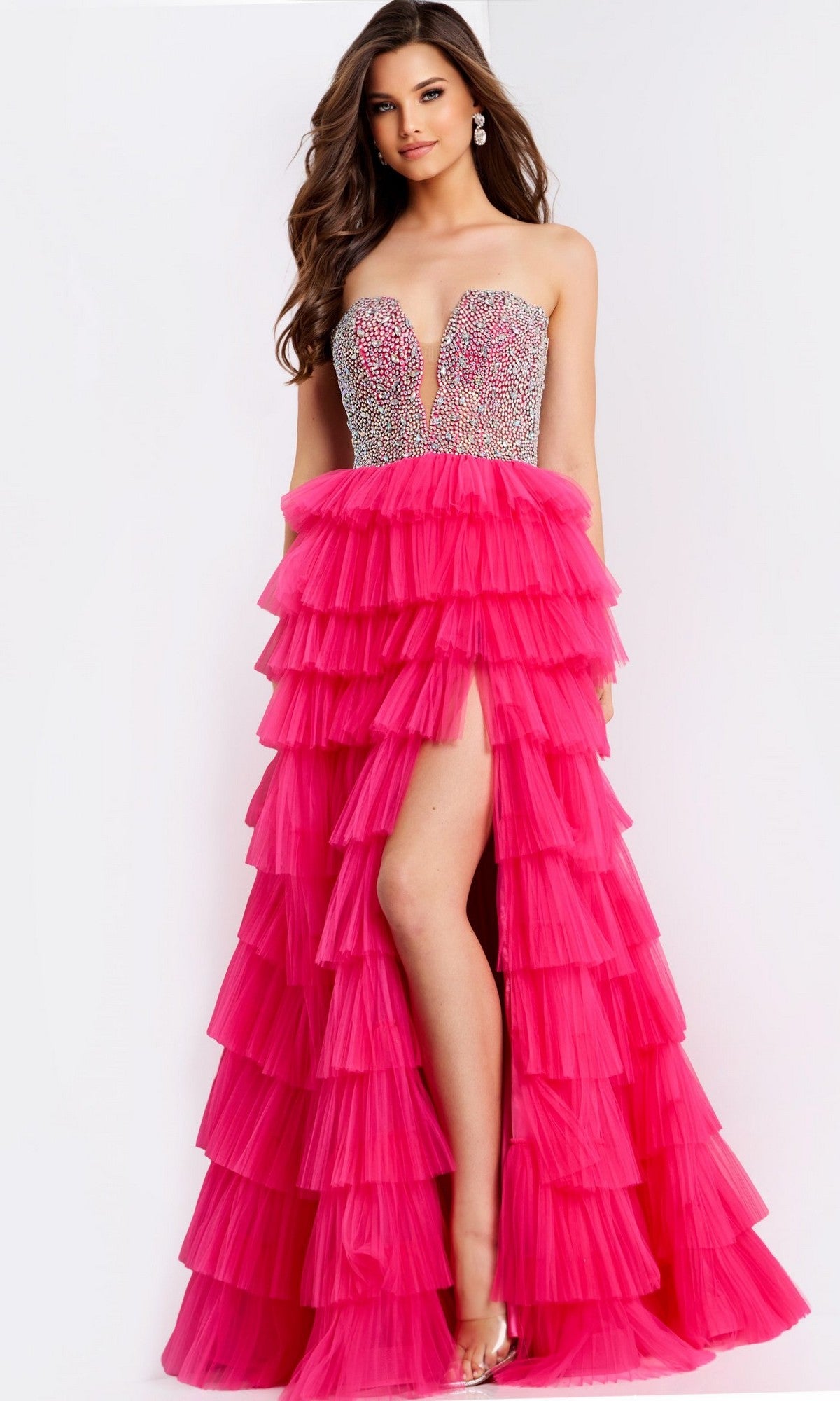 A woman wears the Jovani 44360 long prom dress, featuring a strapless rhinestone corset and a layered hot pink tulle A-line skirt with a high front slit.